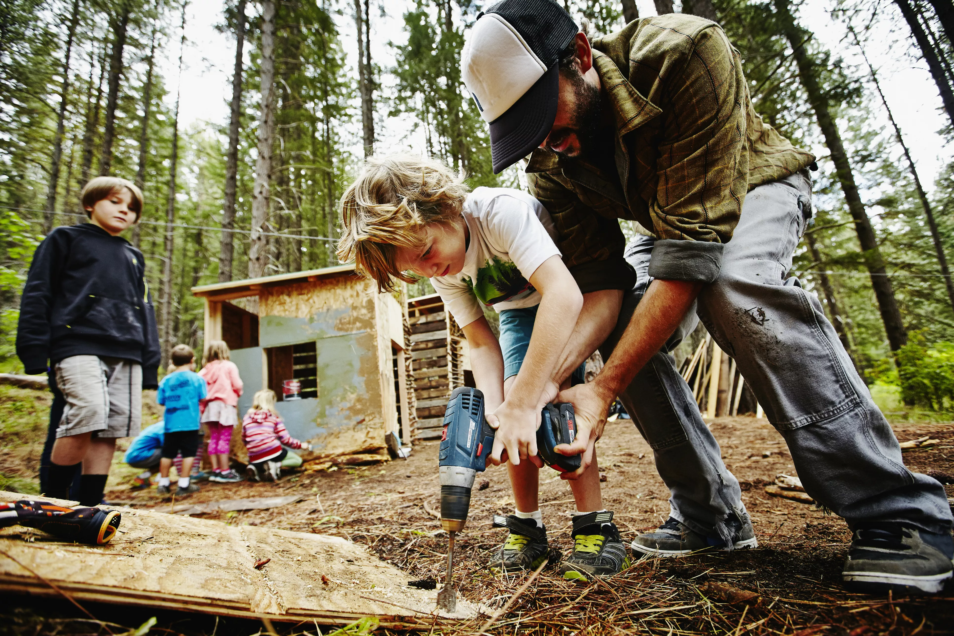 Camp counselor helping young boy use drill